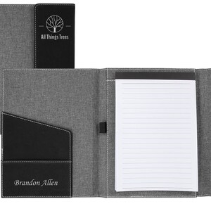 May include: A grey and black fabric folder with a notepad and a pocket. The folder has a black leather flap with the text "All Things Trees" and a tree logo. The pocket has the text "Brandon Allen" in white.