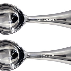 May include: Two silver ice cream scoops with engraved text. The top scoop says "Groom" with a small heart symbol. The bottom scoop says "Bride" with a small heart symbol.