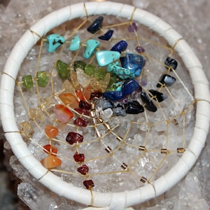 May include: A white dreamcatcher with a beaded web and a variety of colourful gemstones, including red, orange, yellow, green, blue, and purple.