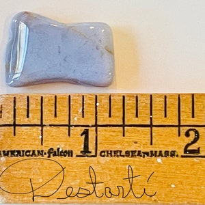 K&ouml;nnte beinhalten: Ein hellblauer Achat-Stein mit einer welligen, unregelm&auml;&szlig;igen Form. Der Stein ist etwa 2,5 cm lang und liegt auf einem Holzlineal mit Zentimeter-Markierungen.