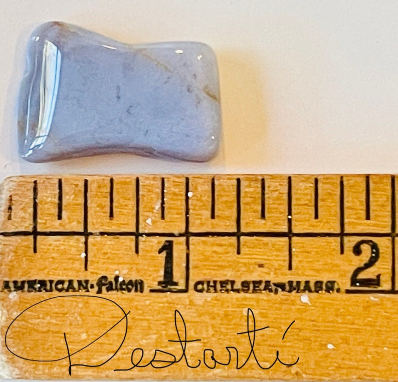 K&ouml;nnte beinhalten: Ein hellblauer Achat-Stein mit einer welligen, unregelm&auml;&szlig;igen Form. Der Stein ist etwa 2,5 cm lang und liegt auf einem Holzlineal mit Zentimeter-Markierungen.