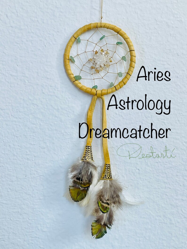 K&ouml;nnte beinhalten: Aries Astrologie Traumf&auml;nger. Dieser handgefertigte Traumf&auml;nger hat einen gelben, lederumwickelten Reifen mit einem gewebten Netz, verziert mit gr&uuml;nen und klaren Edelsteinen. Zwei gelbe Lederriemen h&auml;ngen darunter, verziert mit Federn und dekorativen Metallakzenten. Der Text "Aries Astrology Dreamcatcher" ist sichtbar.