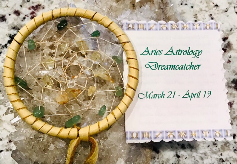 K&ouml;nnte beinhalten: Aries-Astrologie-Traumf&auml;nger mit hellbraun gewebtem Rahmen, gef&uuml;llt mit einem Netz aus Schnur und Edelsteinen. Der Traumf&auml;nger ist mit gr&uuml;nen und gelben Steinen verziert. Eine wei&szlig;e Karte mit gr&uuml;nem Text lautet "Aries Astrology Dreamcatcher, March 21 - April 19."