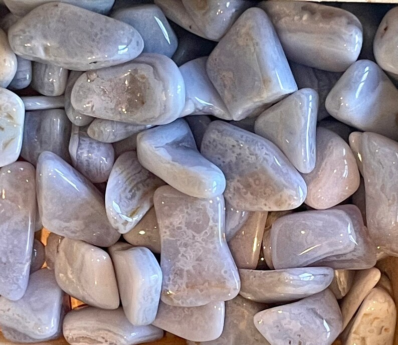 K&ouml;nnte beinhalten: Eine Sammlung von blauen Achat-Trommelsteinen. Die Steine sind glatt und poliert und haben verschiedene Muster und Farben.
