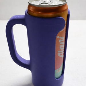 May include: A purple can cooler with a handle, holding an orange and silver can. The can has the word "Alani" printed on it. The cooler is made of a solid material and is designed to keep beverages cold.