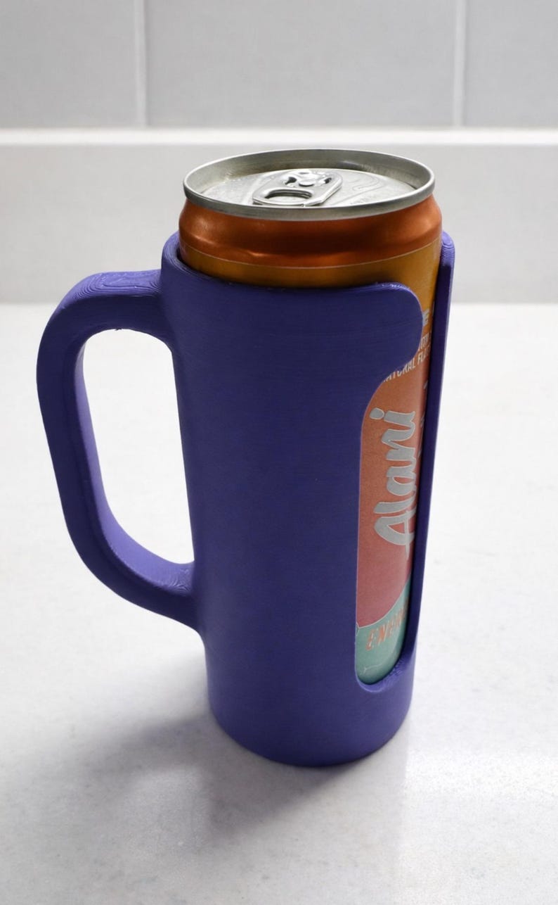 May include: A purple can cooler with a handle, holding an orange and silver can. The can has the word "Alani" printed on it. The cooler is made of a solid material and is designed to keep beverages cold.