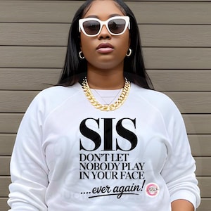 May include: White sweatshirt with the text "SIS DON'T LET NOBODY PLAY IN YOUR FACE...ever again!" in black. The person is wearing white sunglasses and a gold chain necklace.