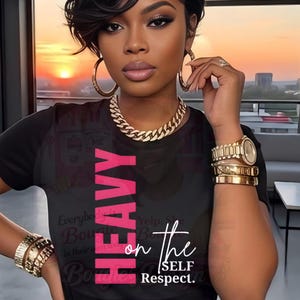 May include: Black t-shirt with the word "HEAVY" in pink and the phrase "on the SELF Respect." in white. The person is wearing gold jewelry, including a chain necklace, hoop earrings, bracelets, and a watch.