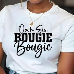Op de afbeelding: Wit T-shirt met de tekst "Ooh Sis, Bougie Bougie" in zwarte letters en blokletters. Het model draagt gouden sieraden en een blauwe jeans.