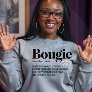 以下が含まれることがあります： 大きな黒い文字で「Bougie」と書かれた、明るい灰色のスウェットシャツ。 「Bougie」の定義が下に印刷されています。 このスウェットシャツは、衣料品ラインの一部です。