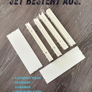 Könnte beinhalten: Ein Set aus weißen Montageteilen, bestehend aus vier Schienensegmenten, zwei flachen rechteckigen Platten und Schrauben. Der Text "SET BESTEHT AUS:" steht oben, gefolgt von einer Liste: "4 SCHIENEN TEILEN", "PASSENDEN SCHRAUBEN", "1 MONTAGEPLATTEN" und "ABSTANDSCLIP".