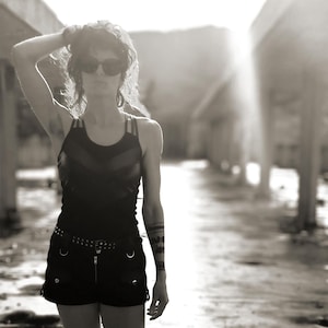 Puede incluir: Un top negro con diseño de chevrón, combinado con shorts negros con cierre de cremallera y cinturón con tachuelas. La persona lleva gafas de sol. La imagen está en escala de grises.