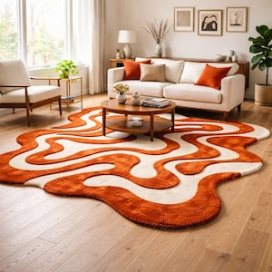 May include: An area rug featuring an irregular, organic shape with a wavy, abstract pattern of burnt orange and cream white. The rug has a thick, plush texture and covers a portion of the light-coloured wooden floor in front of a sofa and chair.