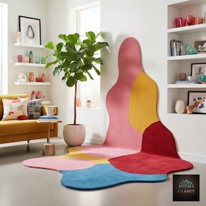 May include: An abstract rug in a living room setting, featuring a flowing design in shades of pink, yellow, red, and blue. The rug's unusual shape and color palette create a modern aesthetic. The room also includes a yellow sofa and a large potted plant.