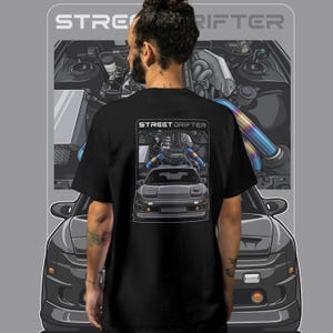 May include: Black t-shirt with a graphic of a car engine and the text "STREET DRIFTER". The design features a detailed illustration of a car engine with blue and gold accents, and a car. The shirt is on a gray background.