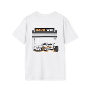 May include: White t-shirt featuring a graphic of a race car with the text "RAUH-Welt" and Japanese text. The car is white with gold wheels and the number 99. A stack of tires is next to the car.