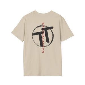 May include: A beige t-shirt featuring a black and red graphic design on the back. The design includes two large black brushstroke "T" shapes inside a black circle, with Japanese text in red.