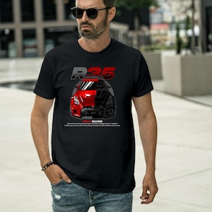 May include: Black t-shirt featuring a graphic of a red and black sports car with the text "R35" and "GODZILLA UNLEASHED". The shirt has a crew neck and short sleeves. The design includes technical details and text.