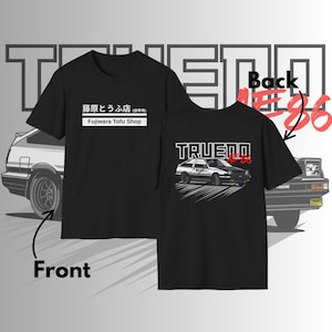 May include: Black t-shirt with a graphic of a car and text. The front of the shirt has Japanese text and "Fujiwara Tofu Shop". The back of the shirt has "TRUENO AE86" with a car graphic. The shirt is displayed with a front and back view.