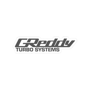Peut inclure: Un autocollant gris et blanc avec le texte "GReddy TURBO SYSTEMS". L'autocollant a une bordure blanche et une forme rectangulaire. Le texte est dans une police stylisée, adapté à diverses surfaces.