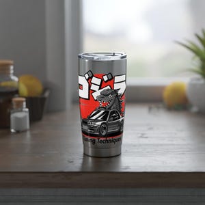 May include: Stainless steel tumbler featuring a Godzilla graphic. The design includes a black and gray Godzilla illustration atop a car, with Japanese text and the words "Tuning Techniques" in white. The tumbler has a silver lid.