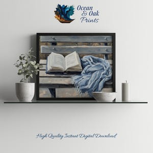 May include: A framed print depicting an open book, a blue scarf, and a bowl on a wooden bench. The artwork uses a neutral colour palette with blue and grey tones. The text "Ocean & Oak Prints" is in the upper right corner.