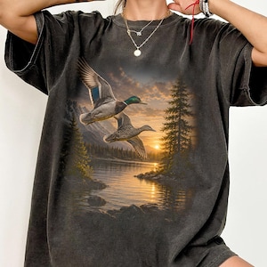 Vintage-inspired wildlife t-shirt featuring realistic flying mallard ducks over a mountain lake at sunrise with retro nature artwork, natural islands, and rustic outdoor aesthetic. Comfort Colors 1717 garment-dyed t-shirt