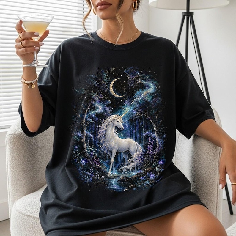 Women’s fantasy graphic t-shirt featuring a  white unicorn standing in an enchanted celestial forest surrounded by glowing moonlight, magical stars, mystical trees, cosmic details, and dreamy fantasy artwork. The design has a vintage-inspired magical aesthetic with fairytale atmosphere, celestial night elements, flowing fantasy illustration, and enchanted woodland scenery printed on a relaxed fit graphic tee for unicorn lovers, fairycore fashion fans, and mystical fantasy style outfits.