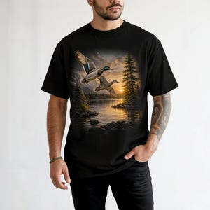 Vintage-inspired wildlife t-shirt featuring realistic flying mallard ducks over a mountain lake at sunrise with retro nature artwork, natural islands, and rustic outdoor aesthetic. Comfort Colors 1717 garment-dyed t-shirt