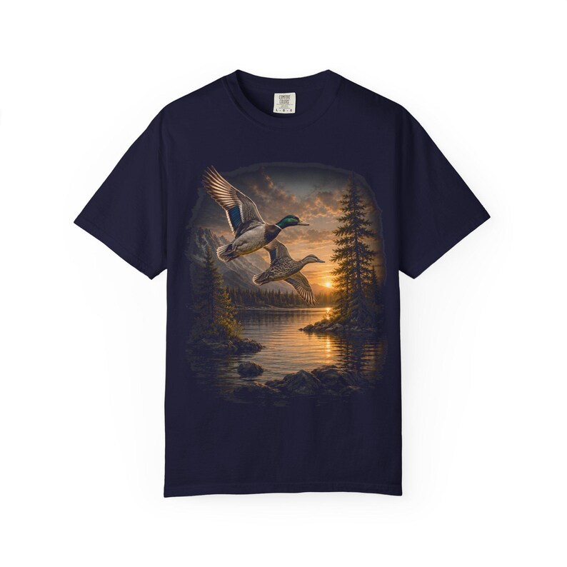 Vintage-inspired wildlife t-shirt featuring realistic flying mallard ducks over a mountain lake at sunrise with retro nature artwork, natural islands, and rustic outdoor aesthetic. Comfort Colors 1717 garment-dyed t-shirt