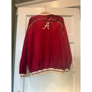 May include: Maroon jacket with white trim and the letter "A" embroidered on the back. The jacket has a ribbed hem and cuffs, and a white collar. The jacket is hanging on a white door.