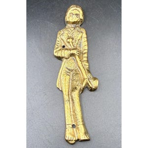 May include: A vintage brass figurine of a person wearing glasses, a suit, and holding a cane and a pipe. The figurine has two holes, one near the head and one near the feet. The brass has a golden color.