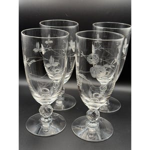 May include: Set of four clear crystal stemmed glasses. Each glass features an etched floral design, with a rose or other flower and leaves. The glasses have a faceted, decorative base and a wide, round foot.