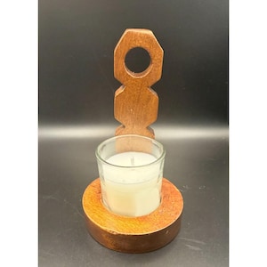 May include: A wooden candle holder with a clear glass votive candle. The candle holder has a round base and a vertical support with a circular opening at the top. The wood has a warm, brown tone.