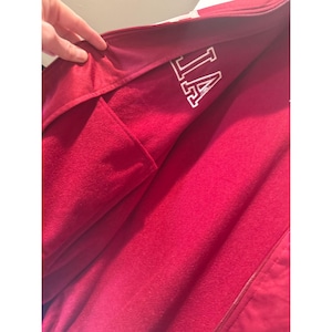 May include: A close-up of a red fleece jacket with a zipper and a pocket. The inside lining is a darker red. The letters "IA" are visible in white on the inside of the jacket.