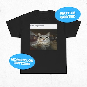 May include: Black t-shirt with a cat meme. The meme shows a grey and white cat with the text "wait im goated" in a white box. There is also a blue oval with the text "WAIT IM GOATED" and another blue oval with the text "MORE COLOR OPTIONS".