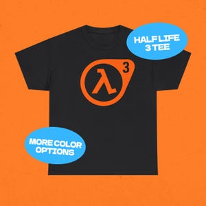 Puede incluir: Camiseta negra con el logo de Half-Life 3 en naranja. El logo es un símbolo lambda dentro de un círculo con el número 3. El texto en la imagen dice "HALF LIFE 3 TEE" y "MORE COLOR OPTIONS".