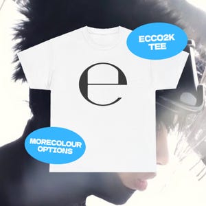May include: White t-shirt with a large black letter "e" on the front. The text "ECCO2K TEE" and "MORECOLOUR OPTIONS" are in blue ovals. The shirt is a crew neck style.