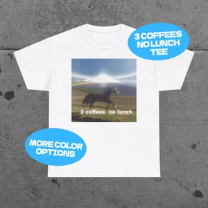 May include: White t-shirt with a graphic of a horse running in front of a mountain. The graphic includes the text "3 coffees no lunch". Additional text on the shirt says "More color options" and "3 coffees no lunch tee".
