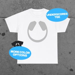 May include: A white short-sleeve t-shirt featuring a centered gray graphic of headphones. The image includes a blue oval with the text UNDERSCORES TEE and a smaller blue oval with the text MORE COLOR OPTIONS next to a miniature black t-shirt icon.