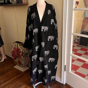 May include: A black duster coat with a white zebra print is displayed on a mannequin. The long, open-front coat has a V-neck and is made of a lightweight fabric. The coat is on a rolling stand. A sign that says "EAT" is hanging in the background.