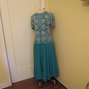 May include: A teal formal dress with a white lace bodice. The dress is on a mannequin and has a skirt that falls to the floor.