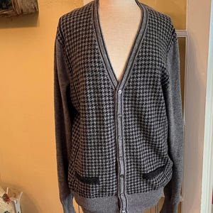 May include: A gray cardigan sweater with a black and gray houndstooth pattern on the front and a solid gray back and sleeves. The sweater has a V-neck, button closure, and two front pockets. The sweater is displayed on a mannequin.