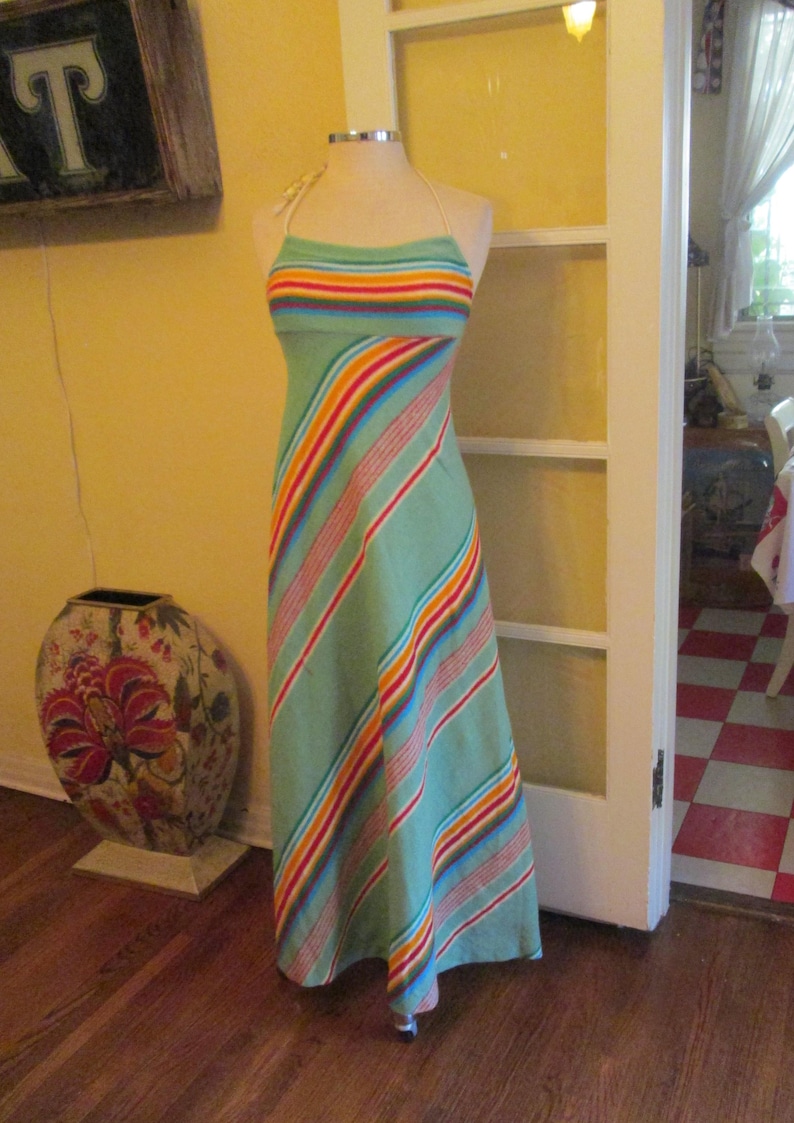 May include: A light green halter dress with colorful horizontal stripes across the bust and diagonal stripes down the skirt. The dress is displayed on a mannequin. The dress is a maxi length.
