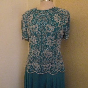 May include: A teal blue dress with a silver beaded floral pattern. The dress has short sleeves and a fitted bodice.