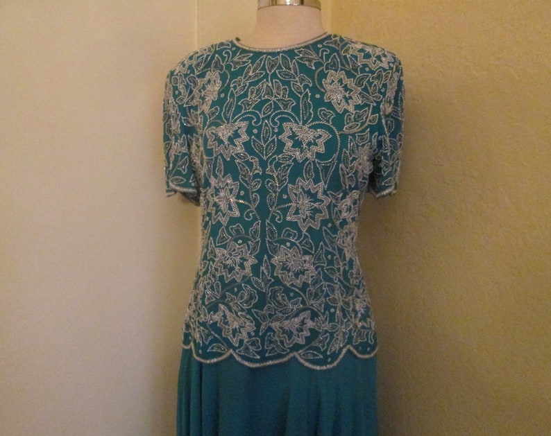 May include: A teal blue dress with a silver beaded floral pattern. The dress has short sleeves and a fitted bodice.