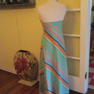 May include: A light green halter dress with diagonal stripes in red, orange, yellow, and blue. The dress is displayed on a mannequin. A decorative vase with floral patterns is in the background.