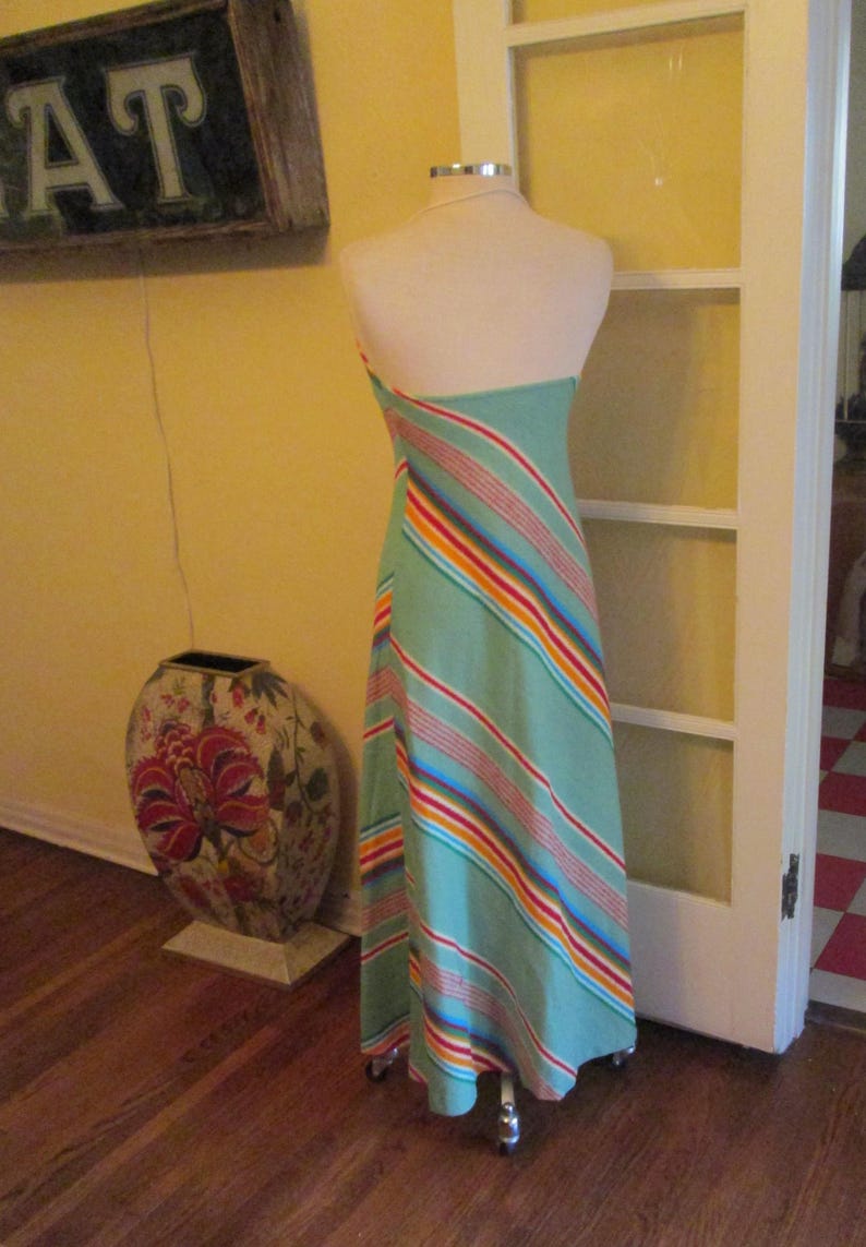 May include: A light green halter dress with diagonal stripes in red, orange, yellow, and blue. The dress is displayed on a mannequin. A decorative vase with floral patterns is in the background.