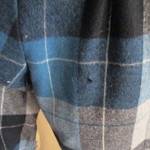 Puede incluir: Primer plano de una tela a cuadros azul, negro y gris. El patr&oacute;n presenta l&iacute;neas que se cruzan creando un dise&ntilde;o en forma de cuadr&iacute;cula. La tela parece ser un material de peso medio, posiblemente lana o una mezcla de lana.