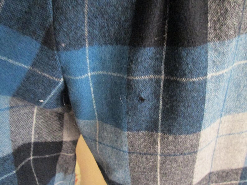 Puede incluir: Primer plano de una tela a cuadros azul, negro y gris. El patr&oacute;n presenta l&iacute;neas que se cruzan creando un dise&ntilde;o en forma de cuadr&iacute;cula. La tela parece ser un material de peso medio, posiblemente lana o una mezcla de lana.
